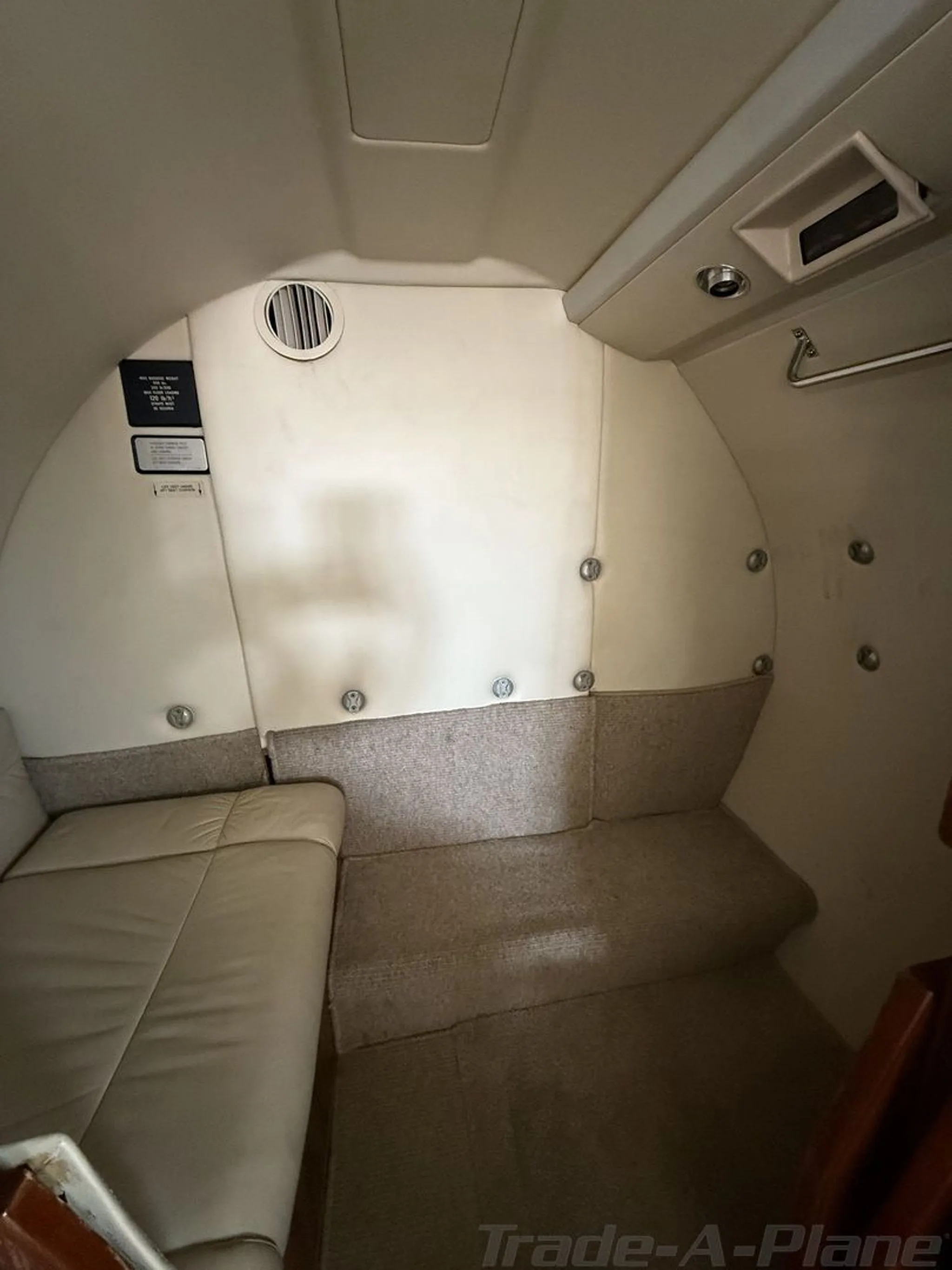 The rear cabin interior of the Cessna Citation jet, N90JJ, featuring a beige bench seat and light-colored walls.