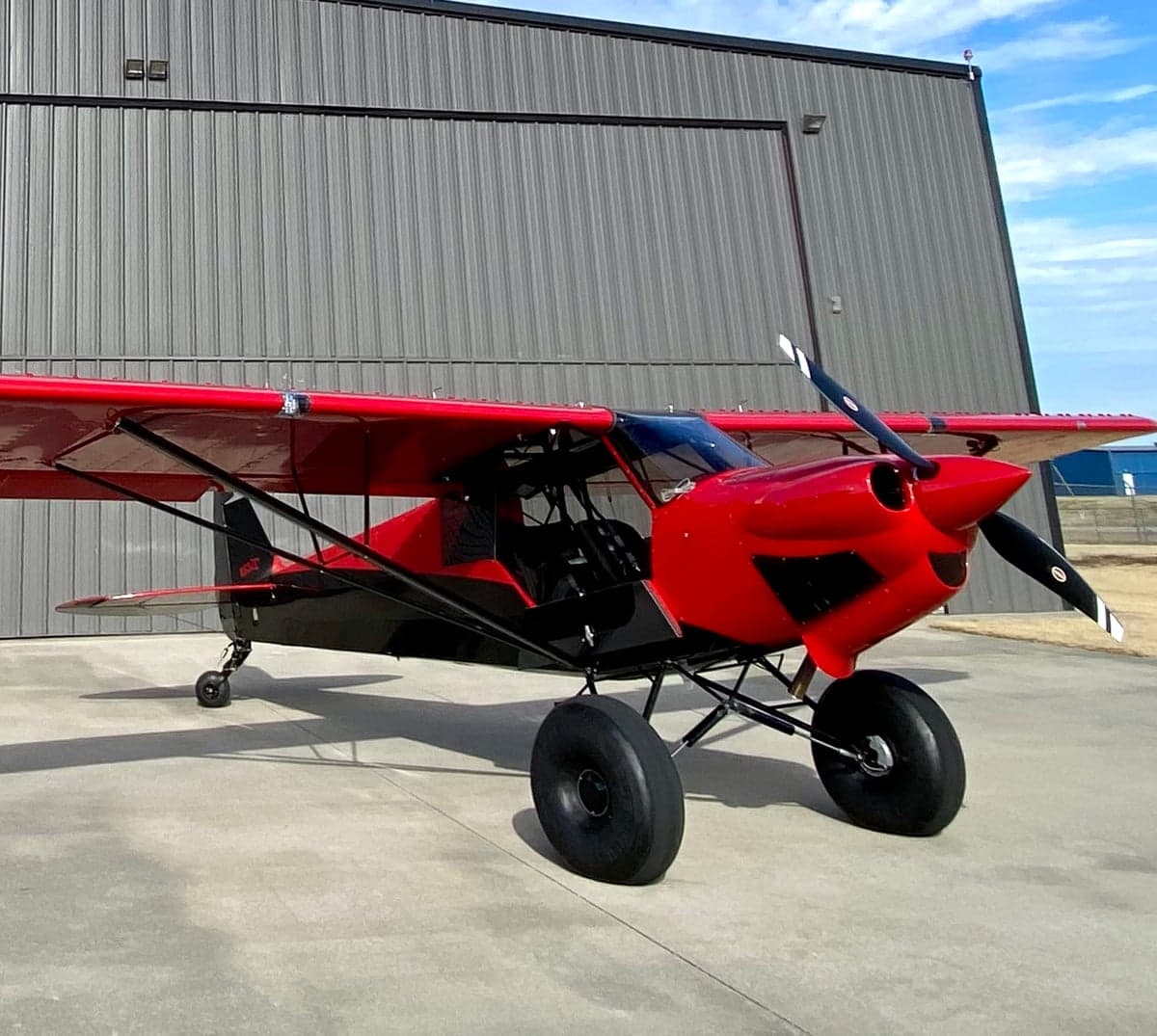 Front side view of the red and black N83ZC aircraft parked outside a hangar.
