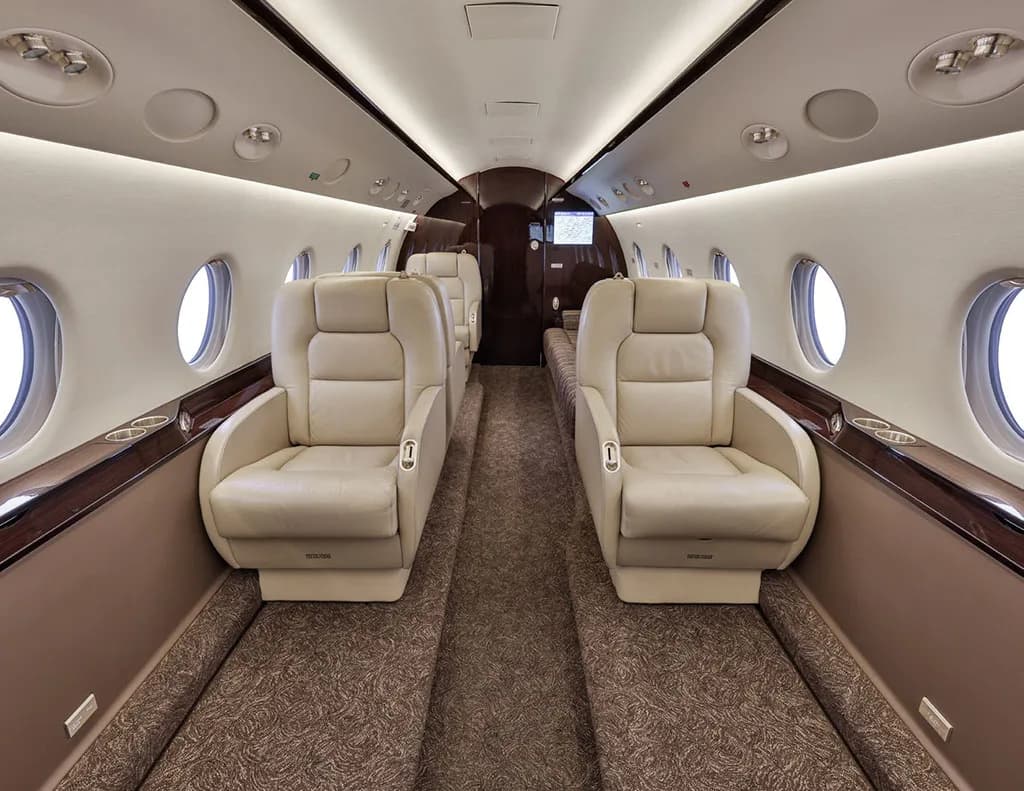The luxurious interior cabin of a private jet, featuring two rows of beige leather seats facing each other.