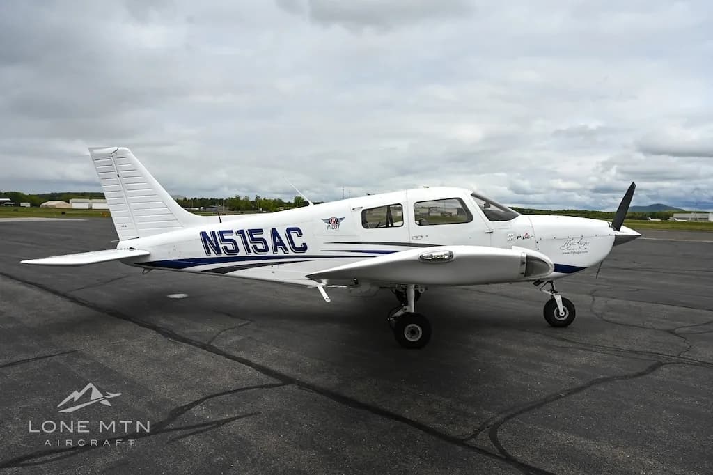 A white single-engine propeller aircraft with blue accents, registration N515AC, parked on an asphalt tarmac under a cloudy sky.