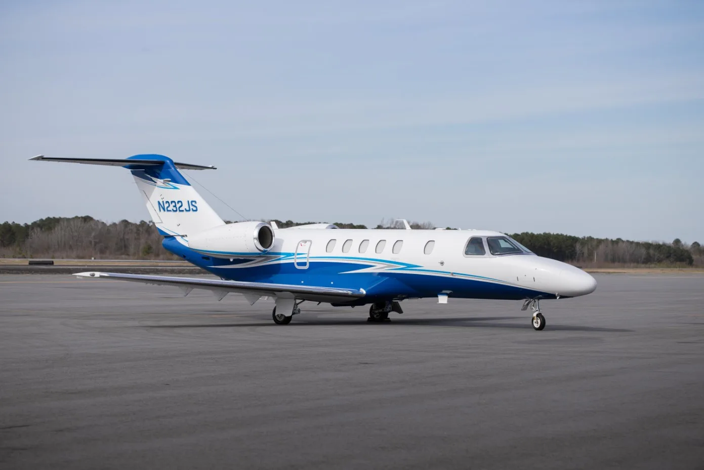 A side view of the white and blue N232JS aircraft on the tarmac.