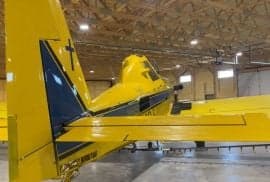 Rear view of a yellow and blue agricultural aircraft in a hangar.