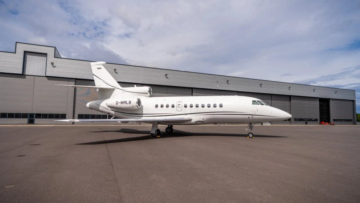 A white Dassault Falcon 7X business jet parked on the tarmac in front of a hangar.