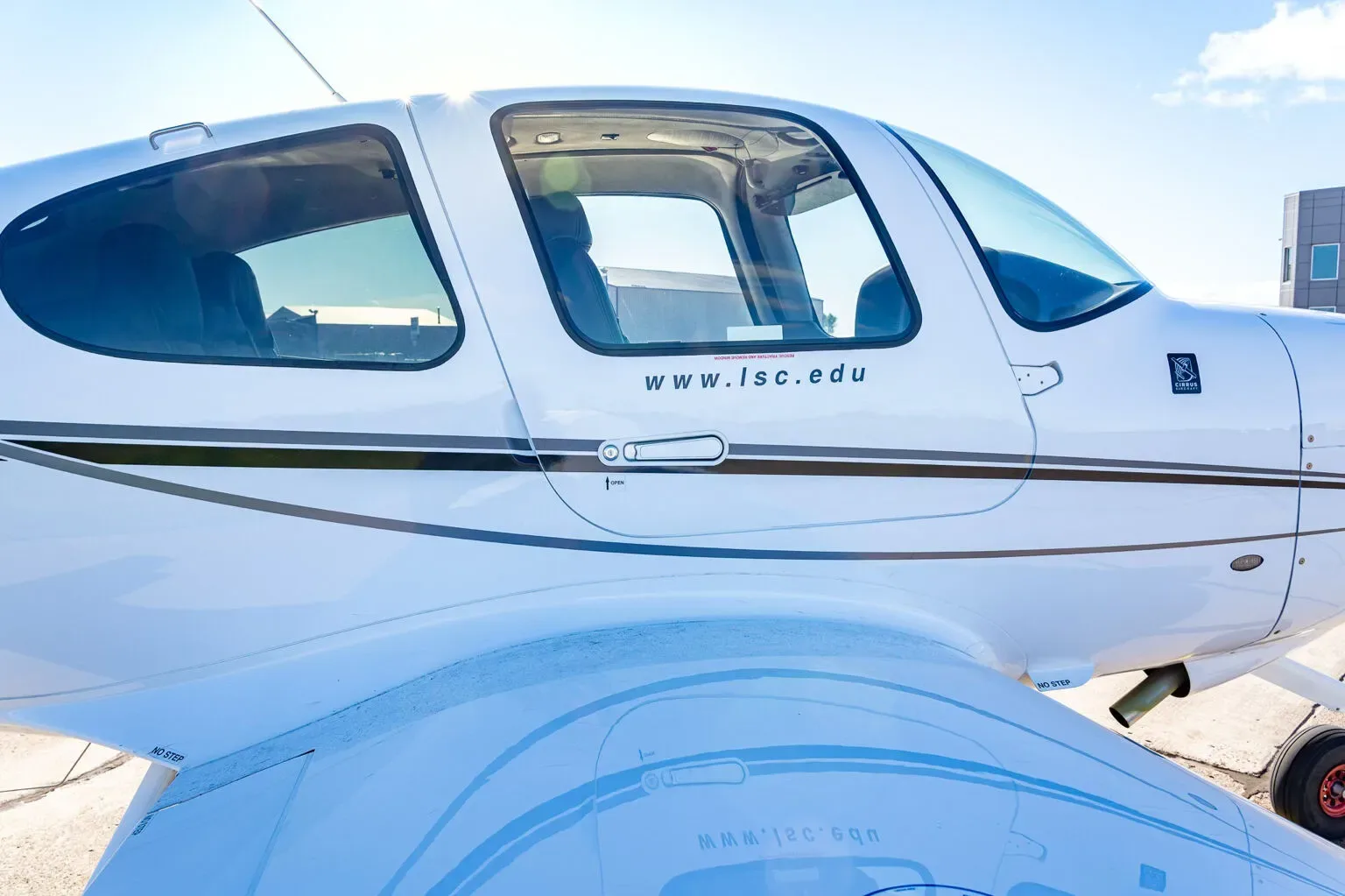 A close-up view of the white fuselage of a Cirrus SR20 aircraft, showing the side windows and "www.lsc.edu" text.