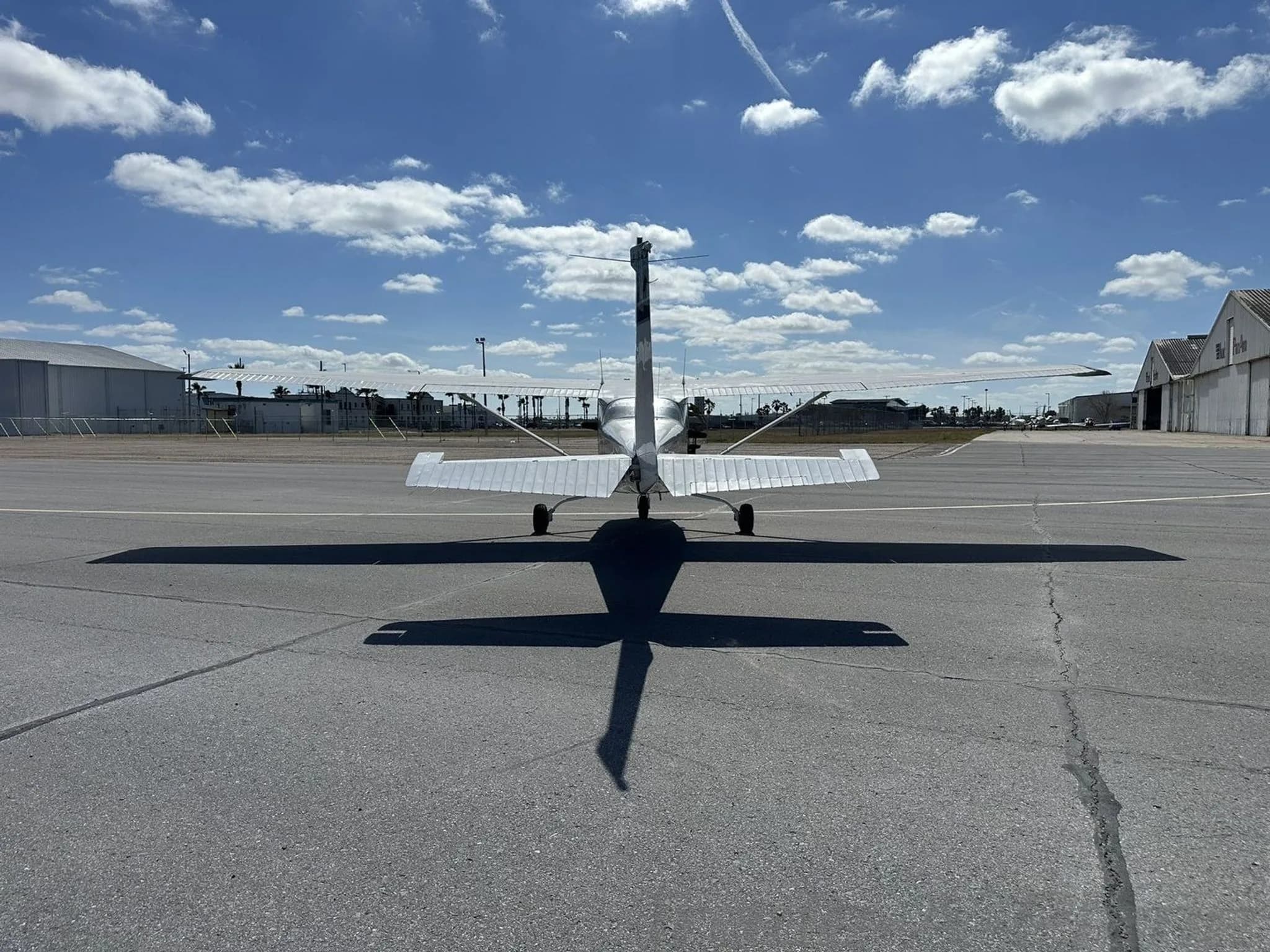 Rear view of the white and dark blue Cessna aircraft N108EA parked on an airport tarmac, casting a long shadow.