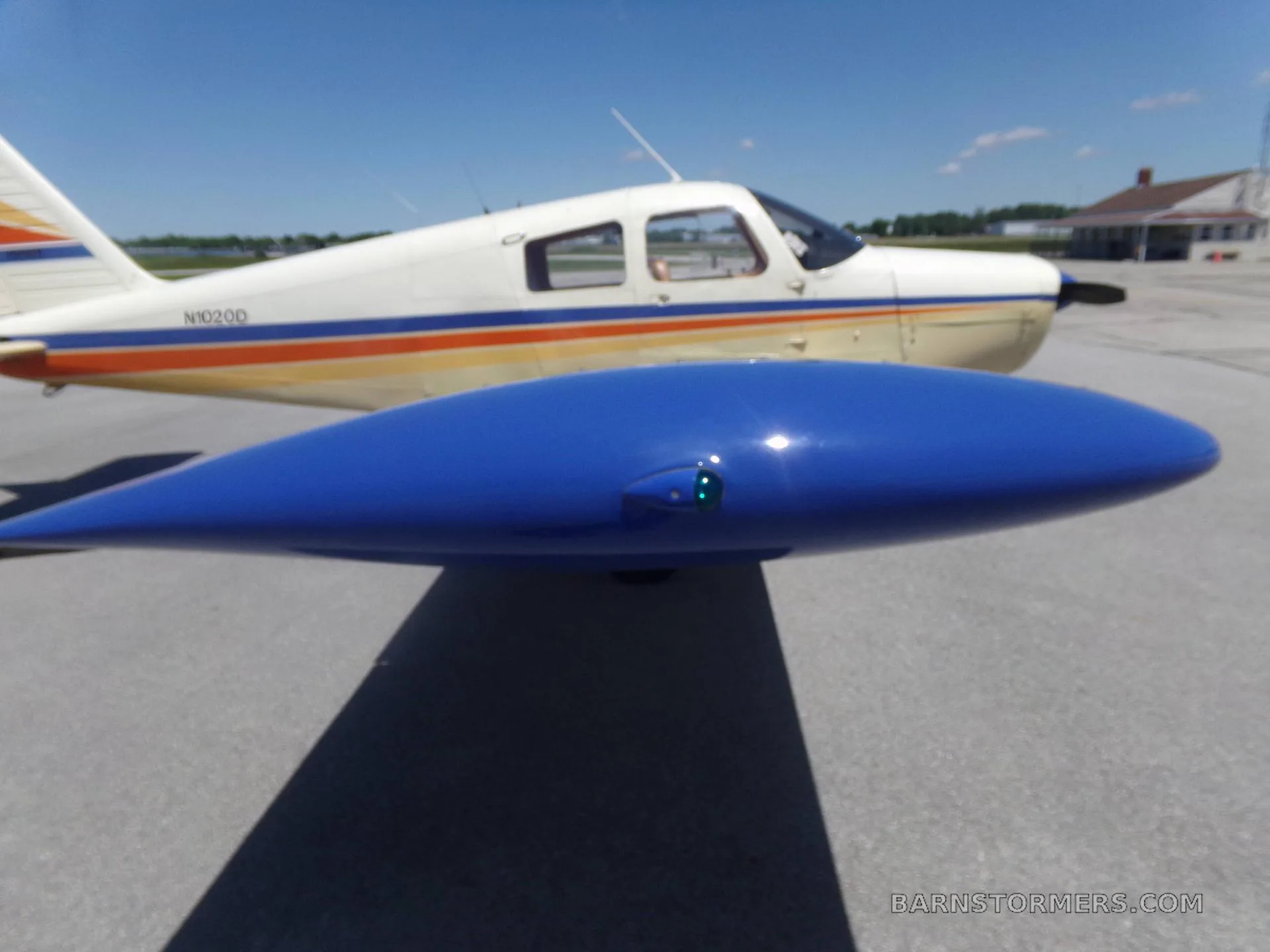 A close-up view of the blue wingtip and part of the fuselage of a white and beige Piper aircraft with N102OD registration.