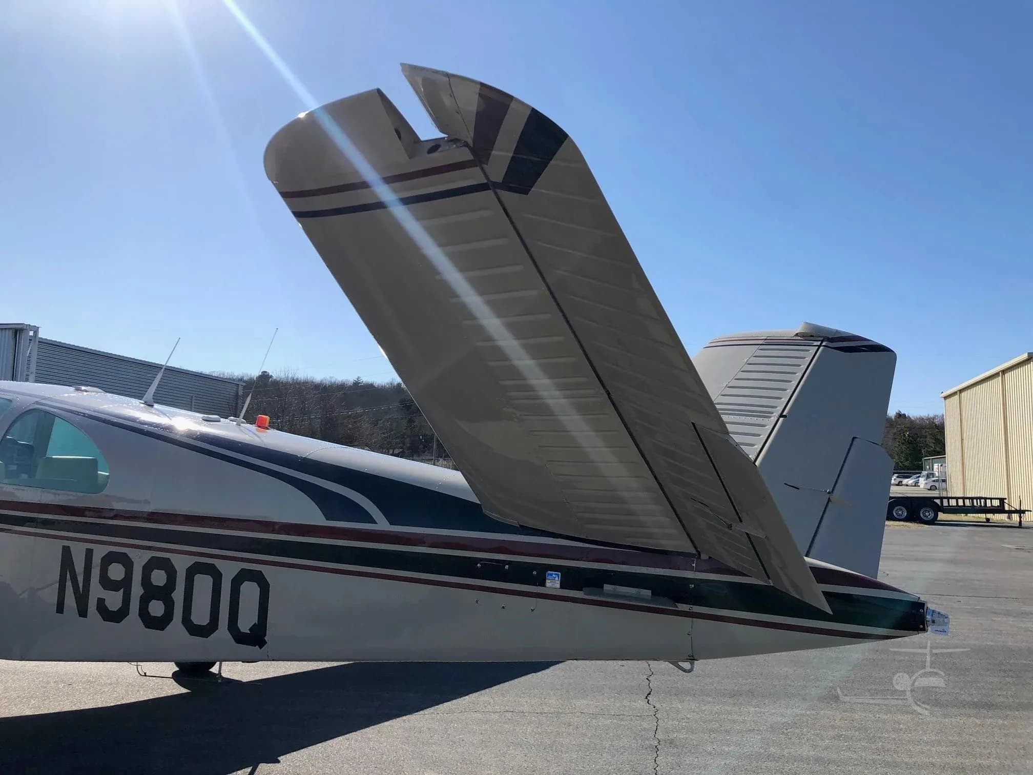 A close-up view of the V-tail of the beige Beechcraft Bonanza N980Q, showing red and black stripes.