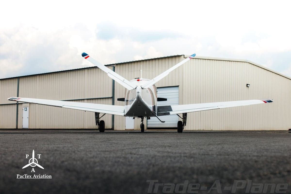 Rear view of a white single-engine aircraft with red and black stripes parked in front of a hangar.