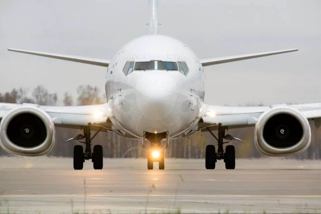 A white passenger jet, possibly a Boeing 737, seen from the front on a runway with its landing lights illuminated.