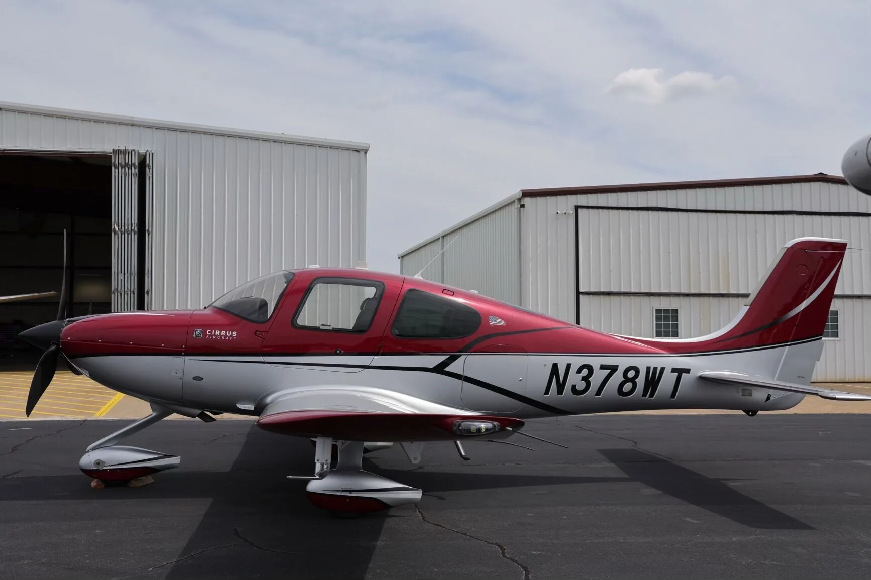 A side view of the red and silver Cirrus SR22T aircraft, N378WT, with its doors closed, parked on an airfield.