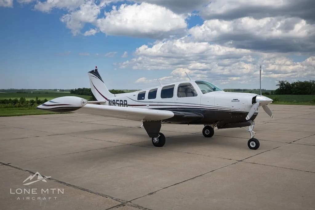 A white and dark grey Beechcraft Baron N85BB parked on a tarmac with a partly cloudy sky.