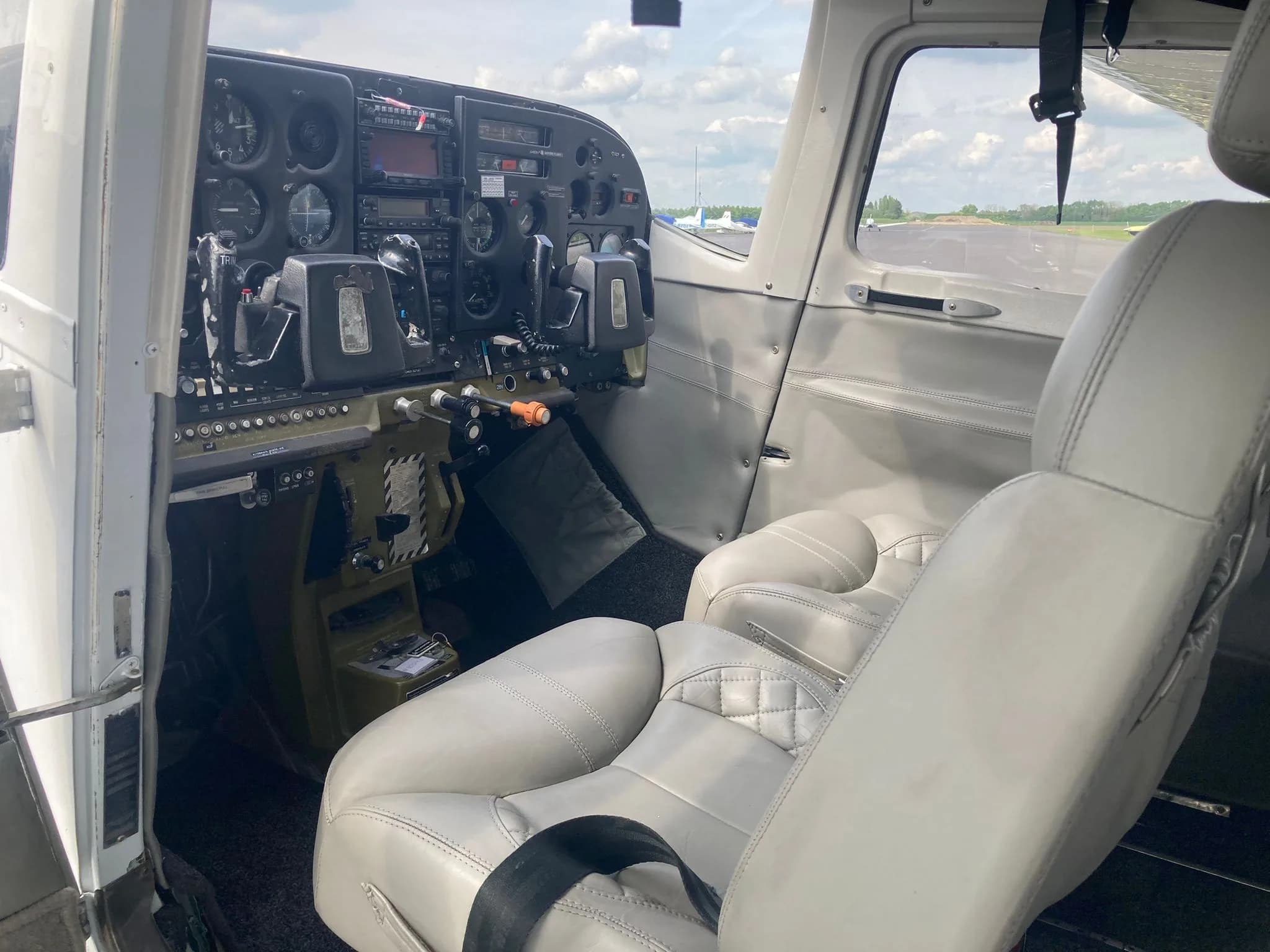 The interior of an aircraft showing the cockpit instruments and light grey leather pilot and co-pilot seats.