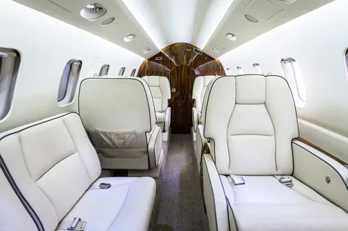 The interior of an aircraft cabin with cream-colored leather seats and a dark wood panel at the rear, looking towards the back.