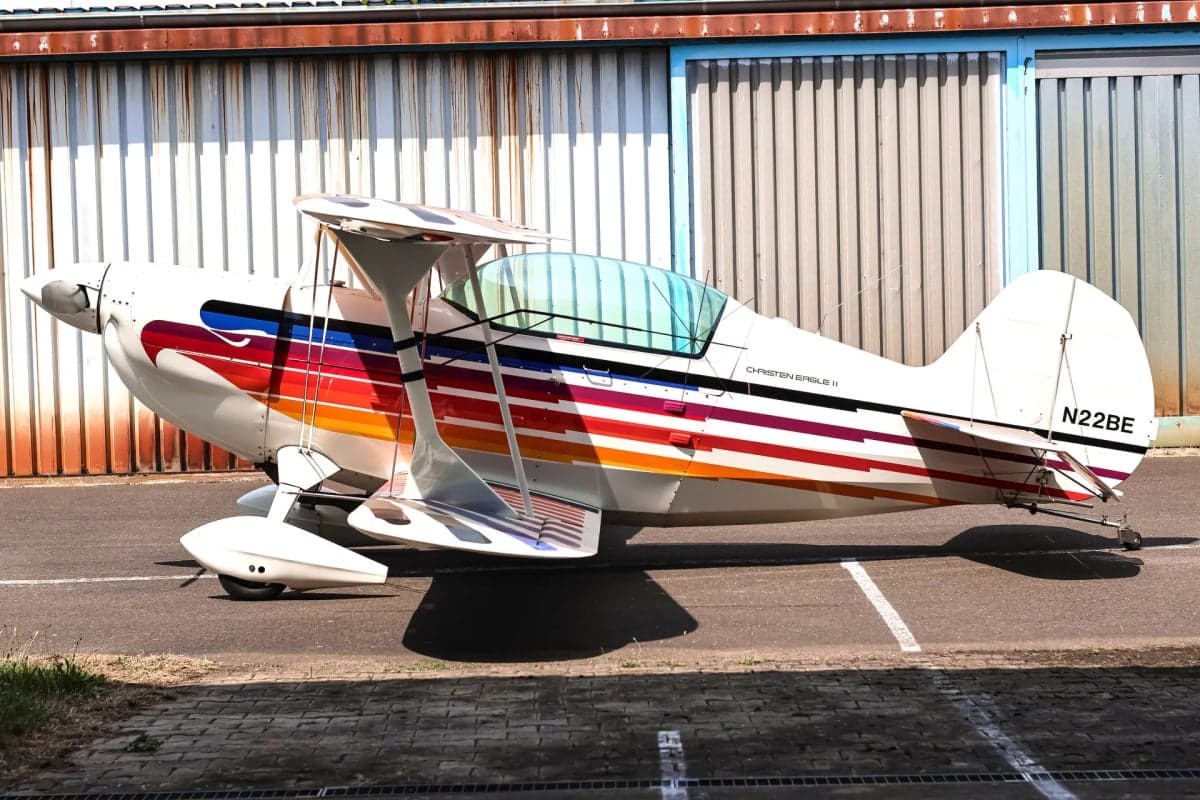Side view of the Christen Eagle II biplane with colorful stripes, parked on the tarmac.