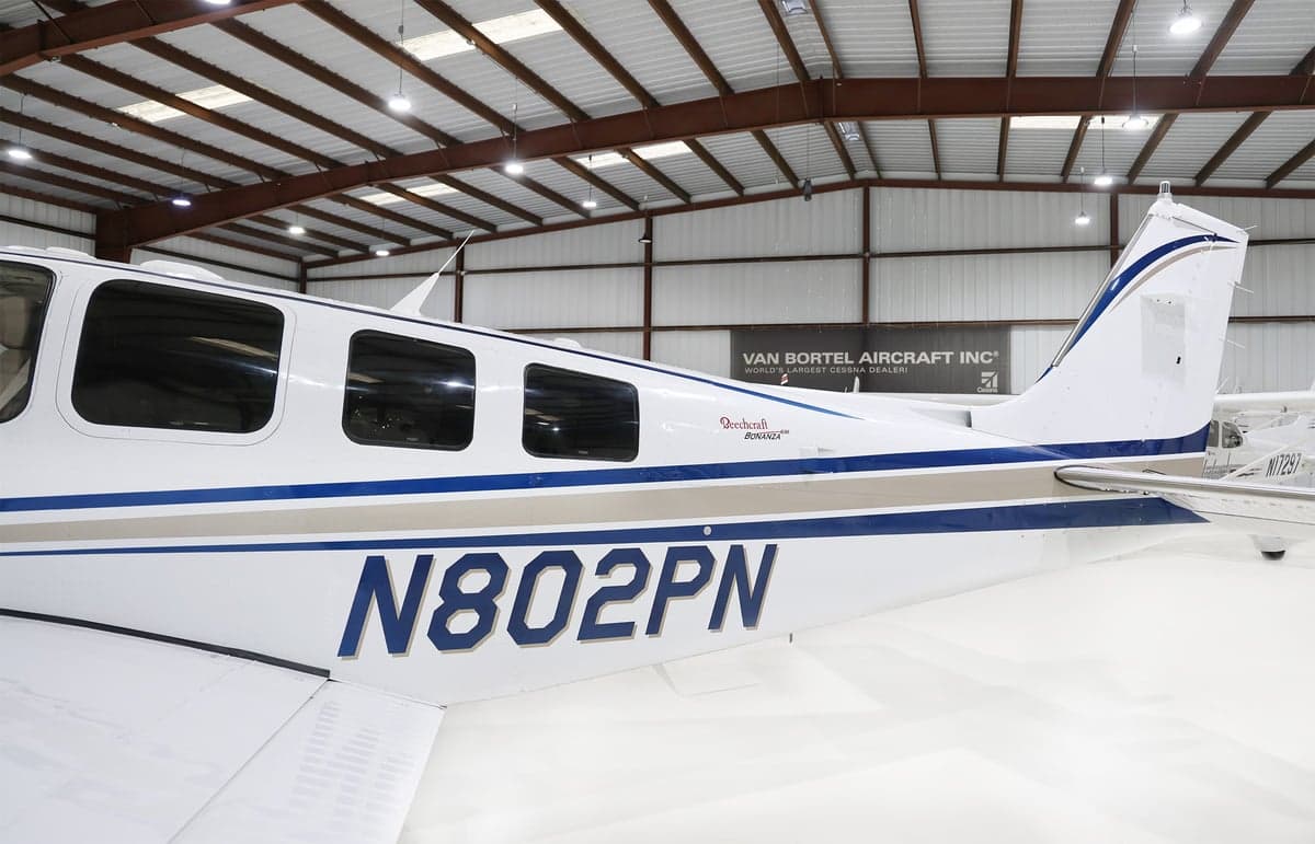 Side view of the tail section of a white Beechcraft Bonanza N802PN with blue and grey stripes.