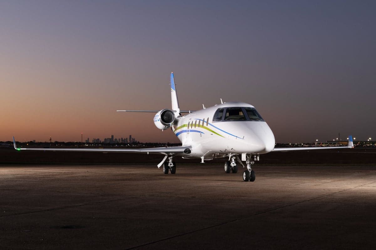 Side view of a white jet with blue and green stripes on the tarmac at dusk.