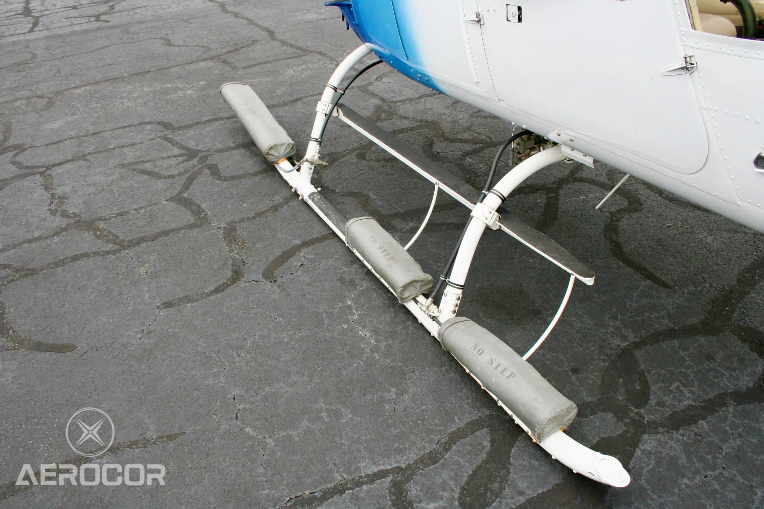 An angled close-up view of the skid landing gear and emergency floats of the blue and white Bell JetRanger III helicopter.