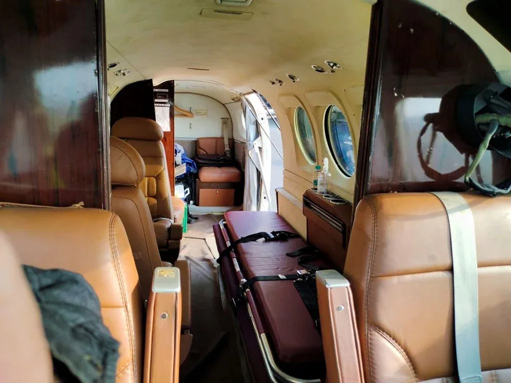 The interior cabin of an aircraft configured with brown leather seats and a medical stretcher in the aisle.
