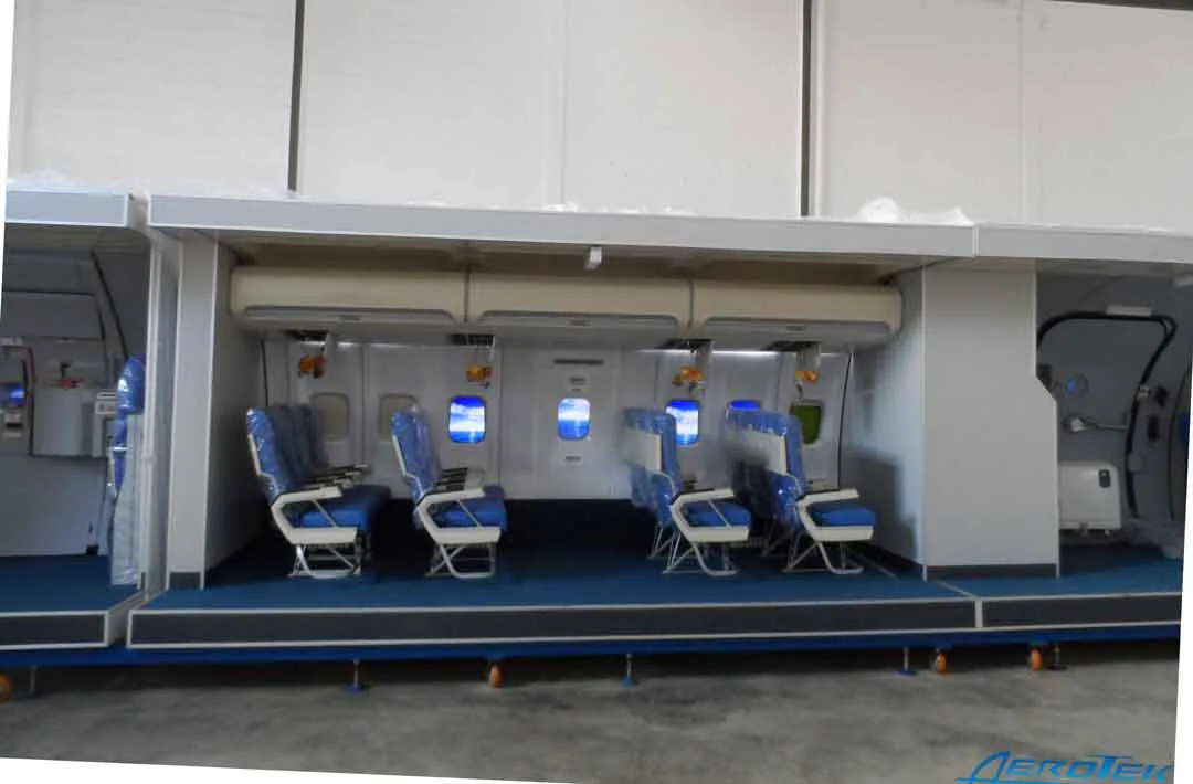 A training mock-up of an aircraft cabin interior with multiple rows of blue seats and windows.