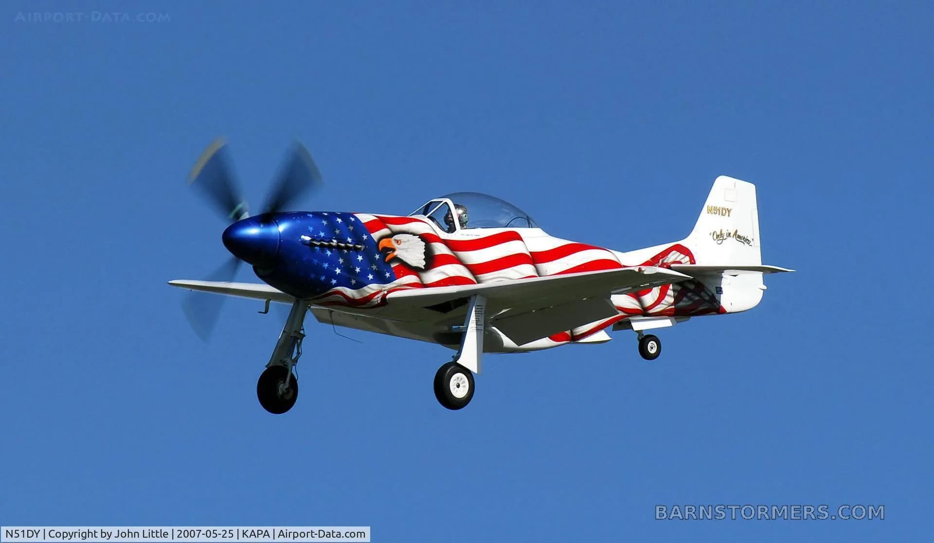 A P-51 Mustang replica, painted with an American flag and eagle, flying against a clear blue sky.
