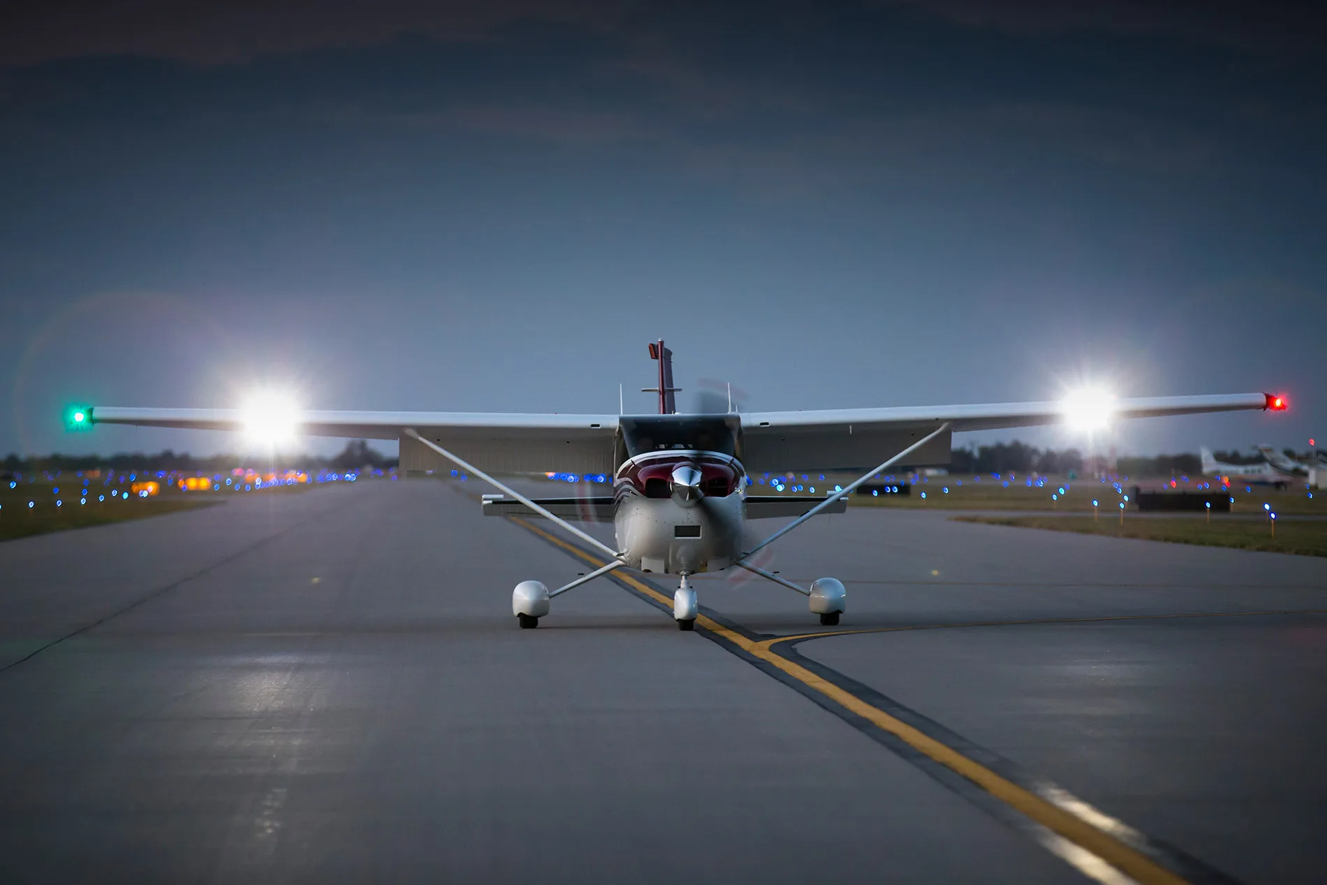 A Cessna 206 Stationair on a runway at dusk, with its landing lights illuminated.