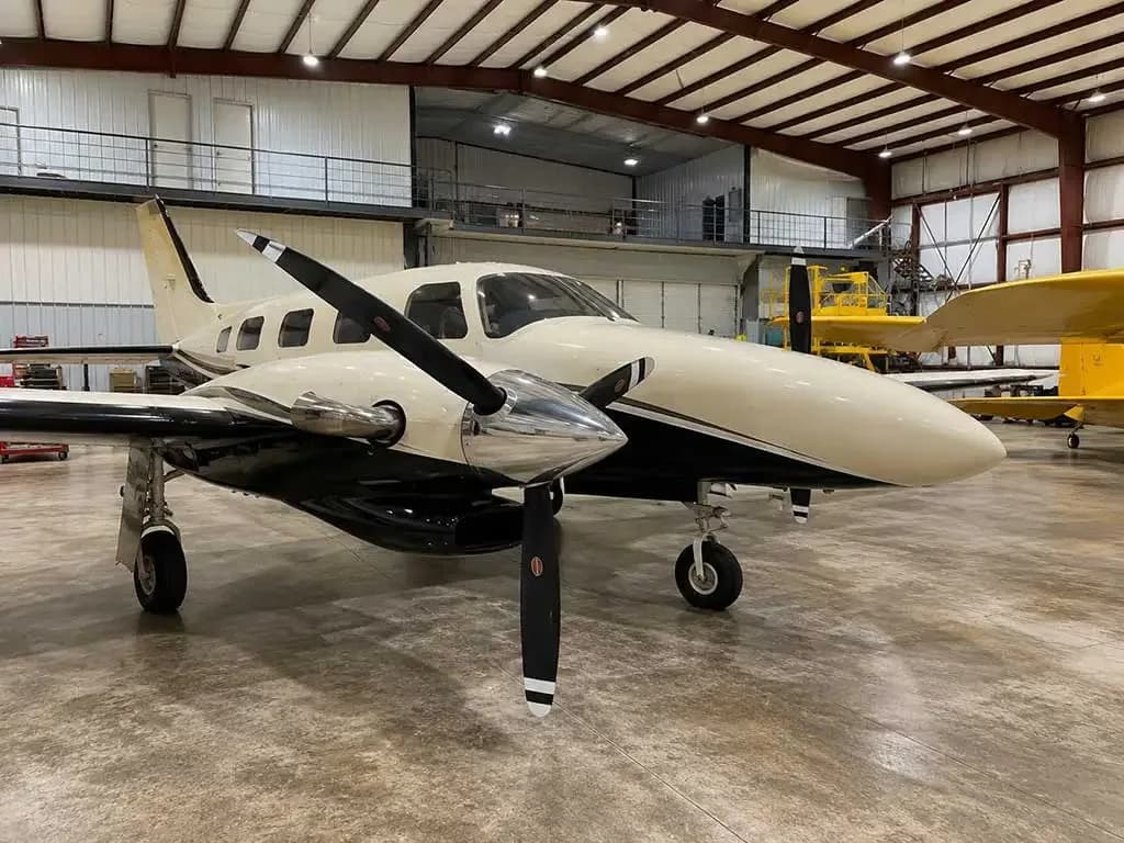 A three-quarter front view of a white and black twin-engine propeller aircraft parked in a hangar.