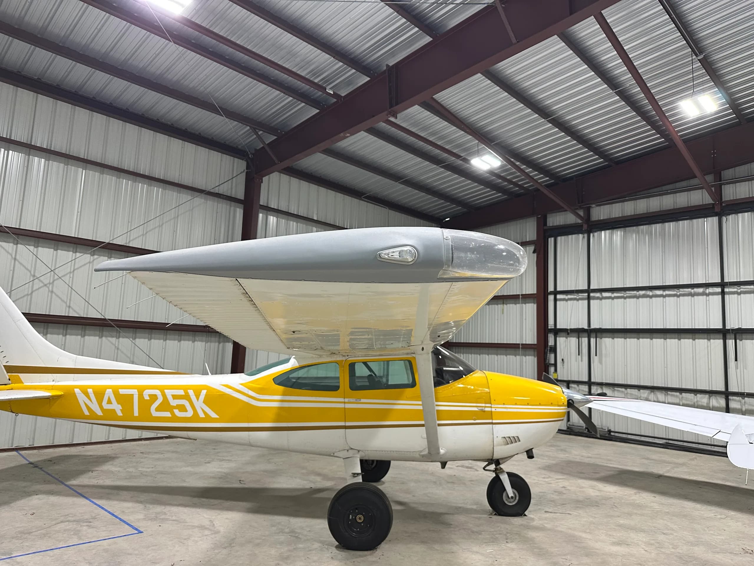 A yellow and white Cessna 172, N4725K, parked in a hangar, viewed from the front-right side.
