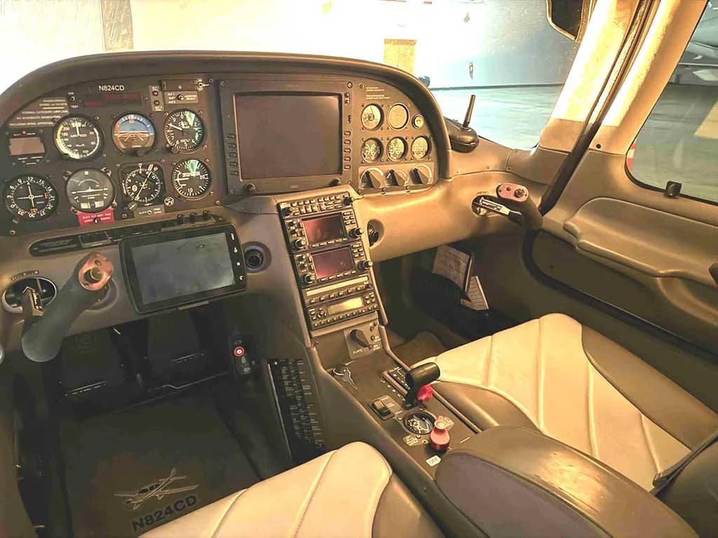 The cockpit of a Cirrus SR20 aircraft, showing the instrument panel with analog gauges and digital displays, and the pilot's controls, with N824CD on the floor mat.