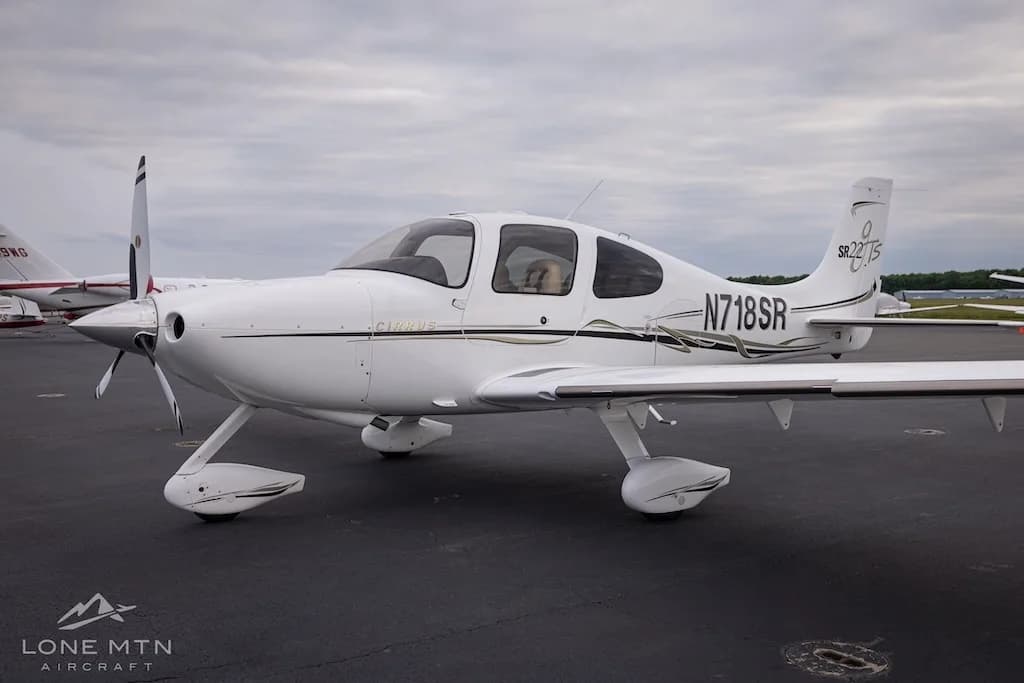 Front-side view of a white Cirrus SR22T aircraft with black and gold accents parked on an asphalt tarmac.