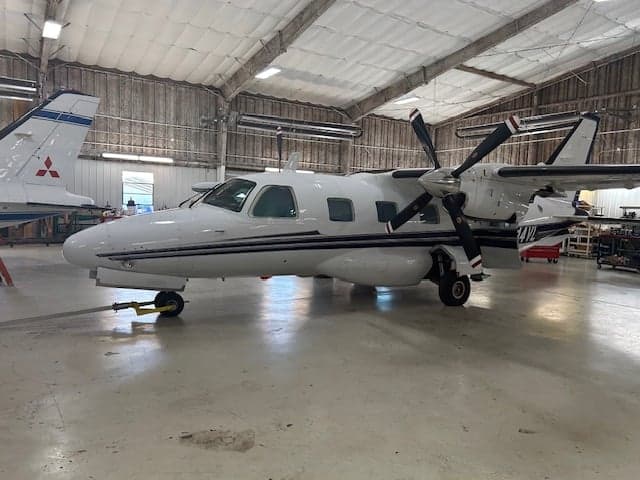 Side view of a white aircraft with black stripes inside a hangar.
