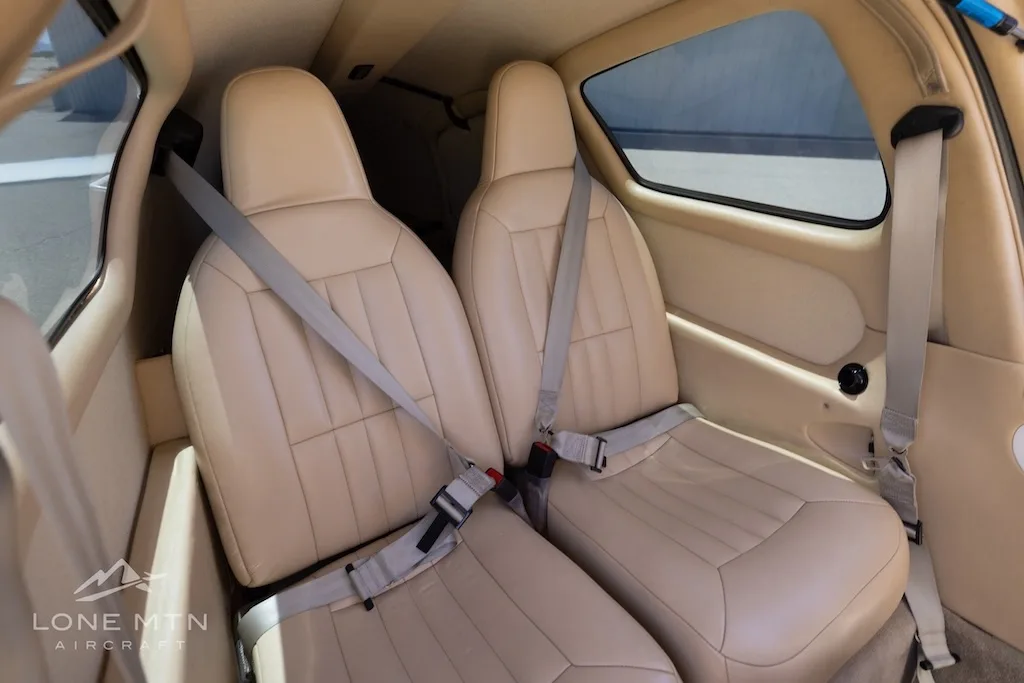 Two tan leather aircraft seats with seatbelts in the rear cabin of a small aircraft.