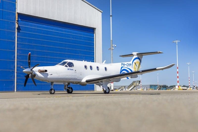 A Pilatus PC-12 aircraft with registration PH-CYP parked on the tarmac in front of a blue hangar.