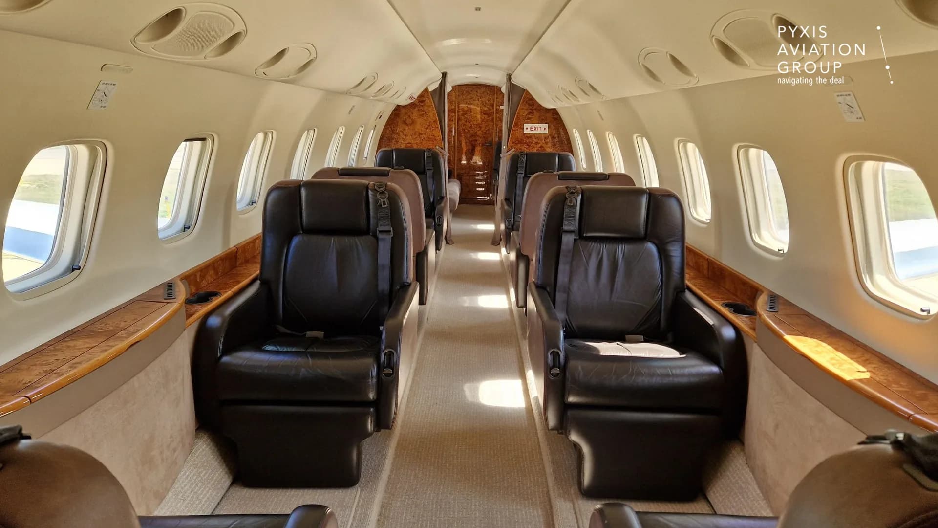 The interior cabin of an aircraft, featuring two rows of dark leather seats and wood paneling.