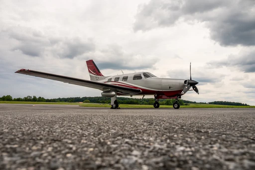 A low-angle view of a silver and red single-engine turboprop aircraft on an asphalt runway under a cloudy sky.