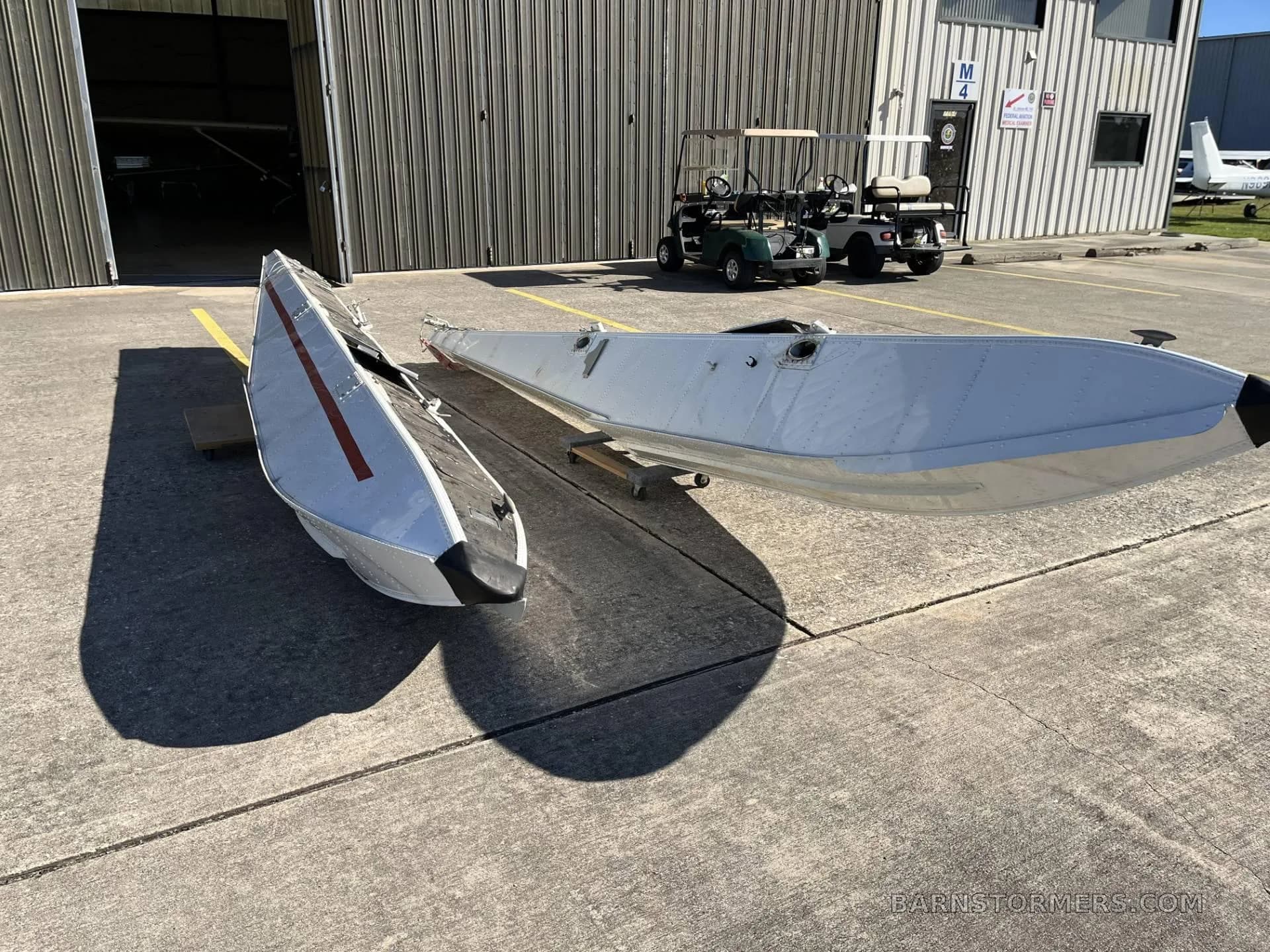 Two white aircraft floats with red stripes and black tips on a concrete apron with a golf cart nearby.