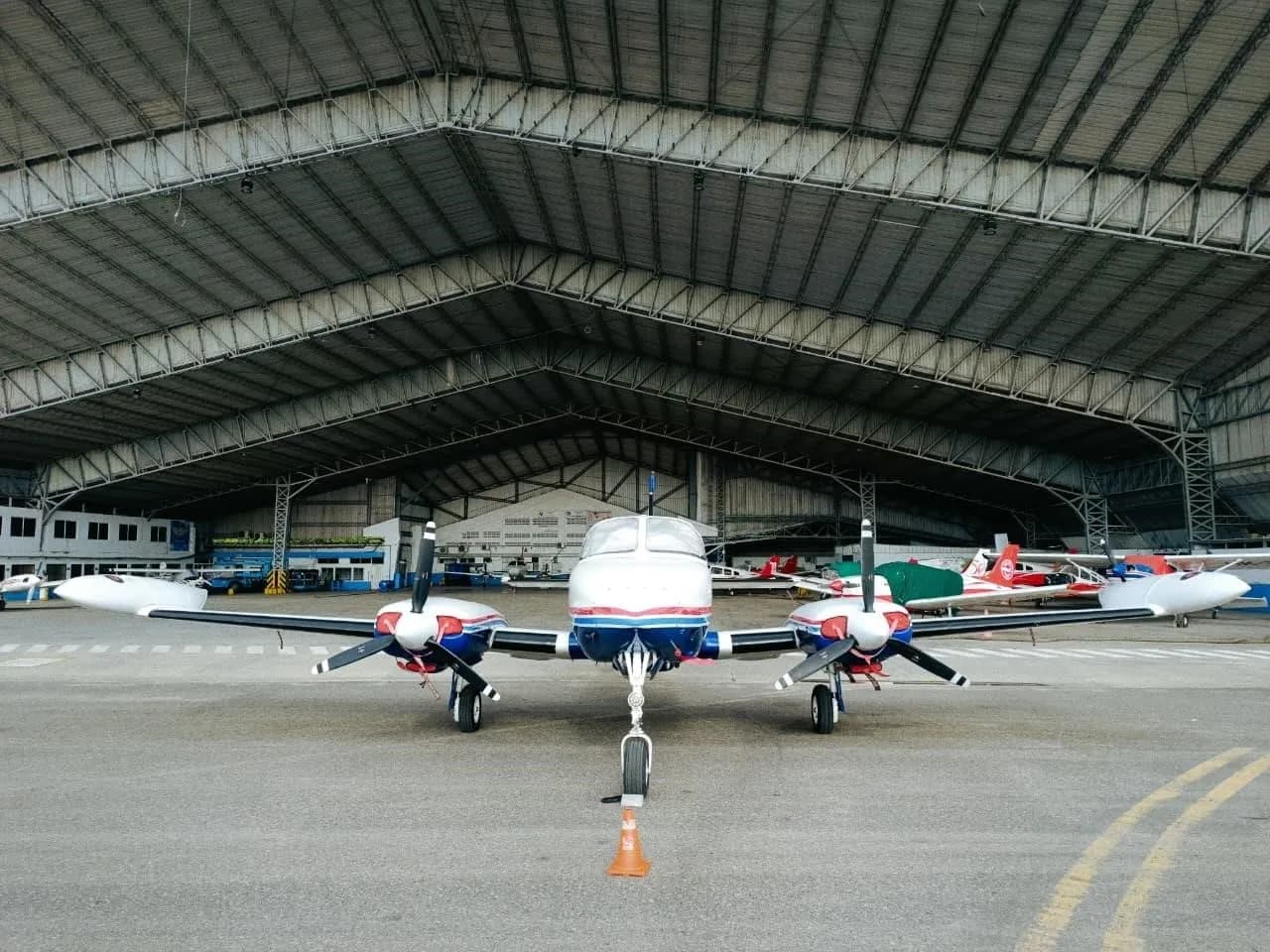 A head-on view of a white and blue Cessna 340 twin-engine aircraft parked in front of a large hangar.