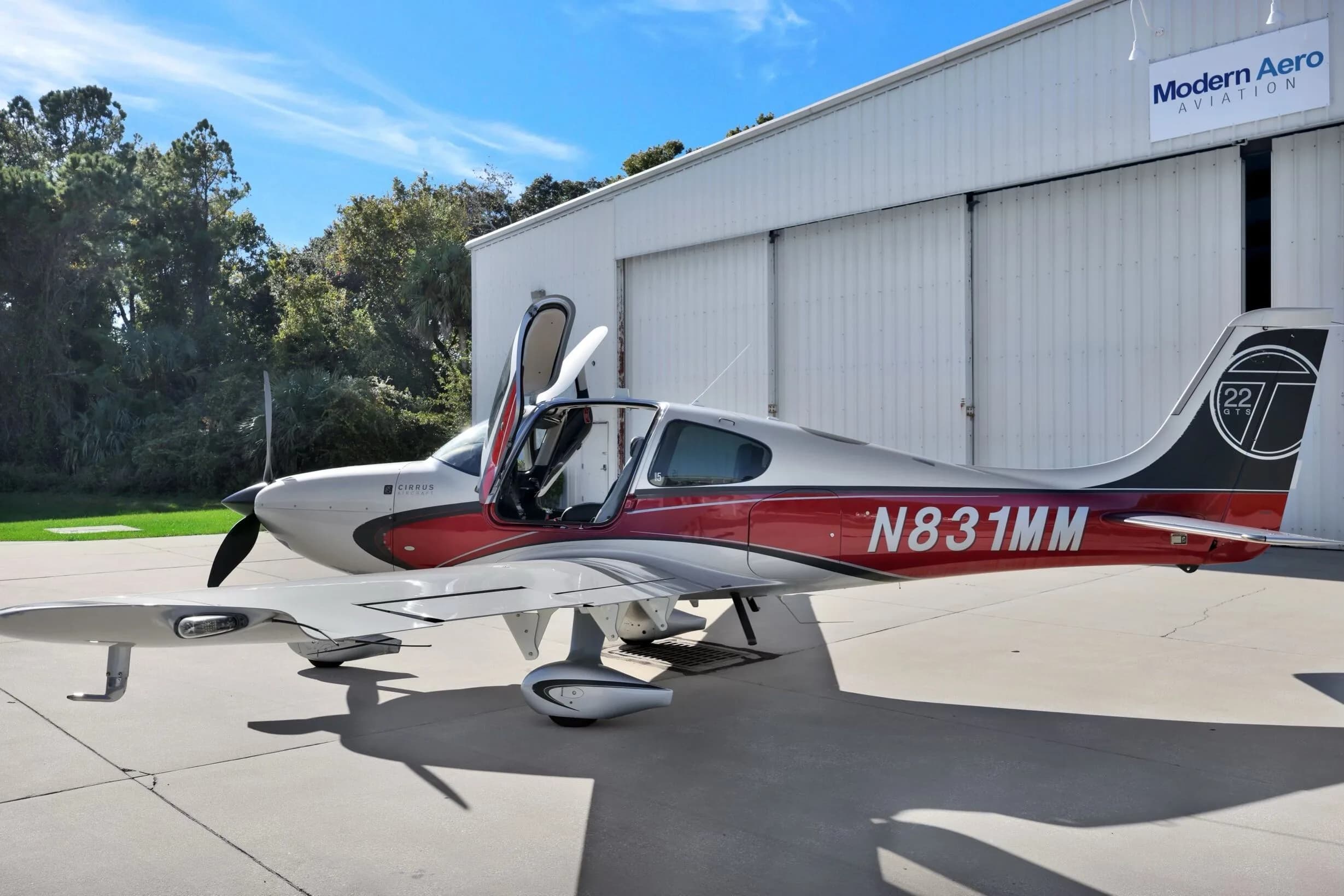 A Cirrus SR22T aircraft with red and silver paint scheme, registration N831MM, parked on an airfield with doors open.
