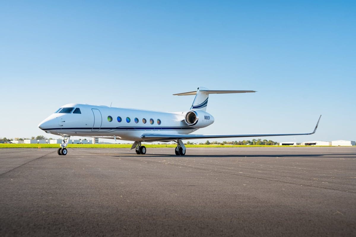 A white Gulfstream jet sits on the tarmac under a clear blue sky.
