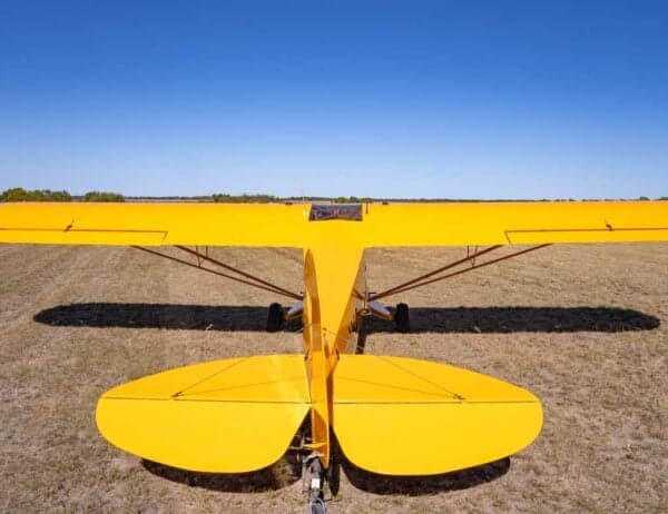 A rear view of the yellow Legend Cub aircraft parked on a grassy field, showing its tail and wings.