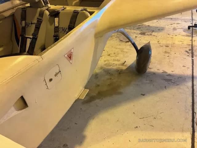 A close-up view of the white fuselage and landing gear of an experimental aircraft inside a hangar.