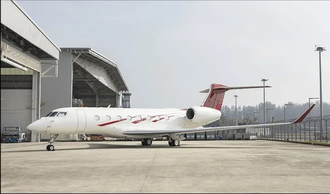 A white Gulfstream business jet with red livery parked outside a hangar on a sunny day.