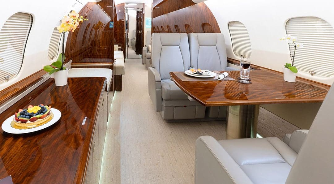A view of the aircraft's interior, showing leather seats, wood trim, and a table set with food and drinks.
