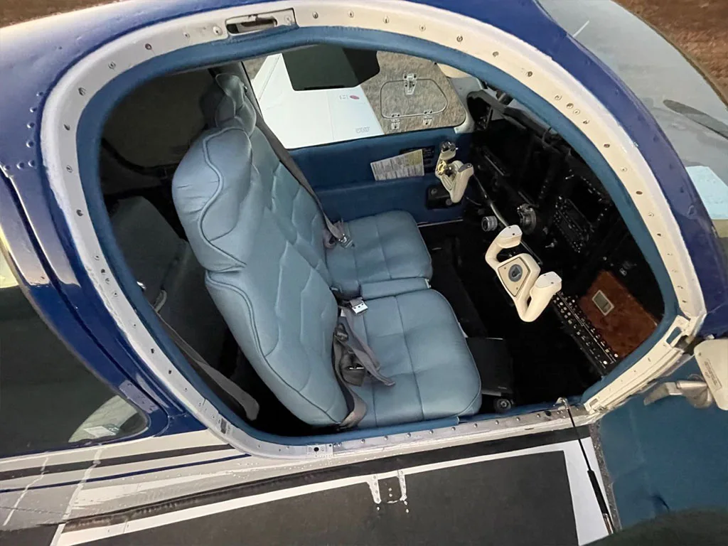 The open door of the aircraft reveals the light blue front seats and a partial view of the cockpit controls.