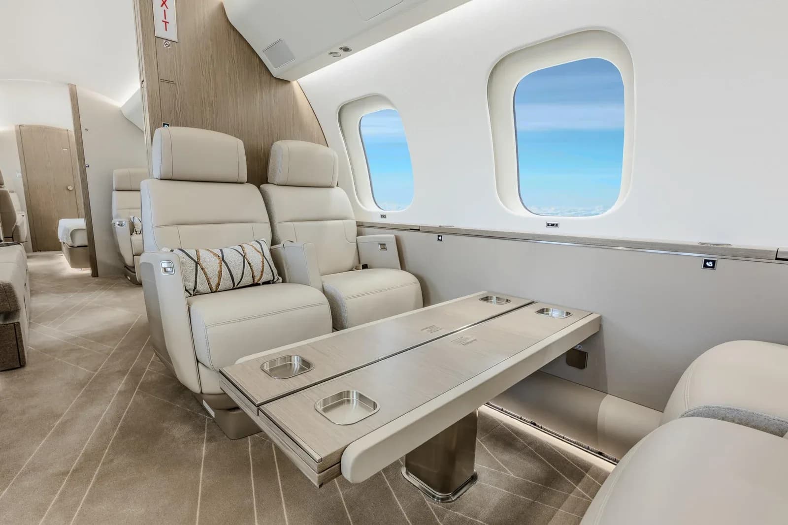 A close-up of two light-colored leather seats facing a wooden table with cupholders in the aircraft cabin.