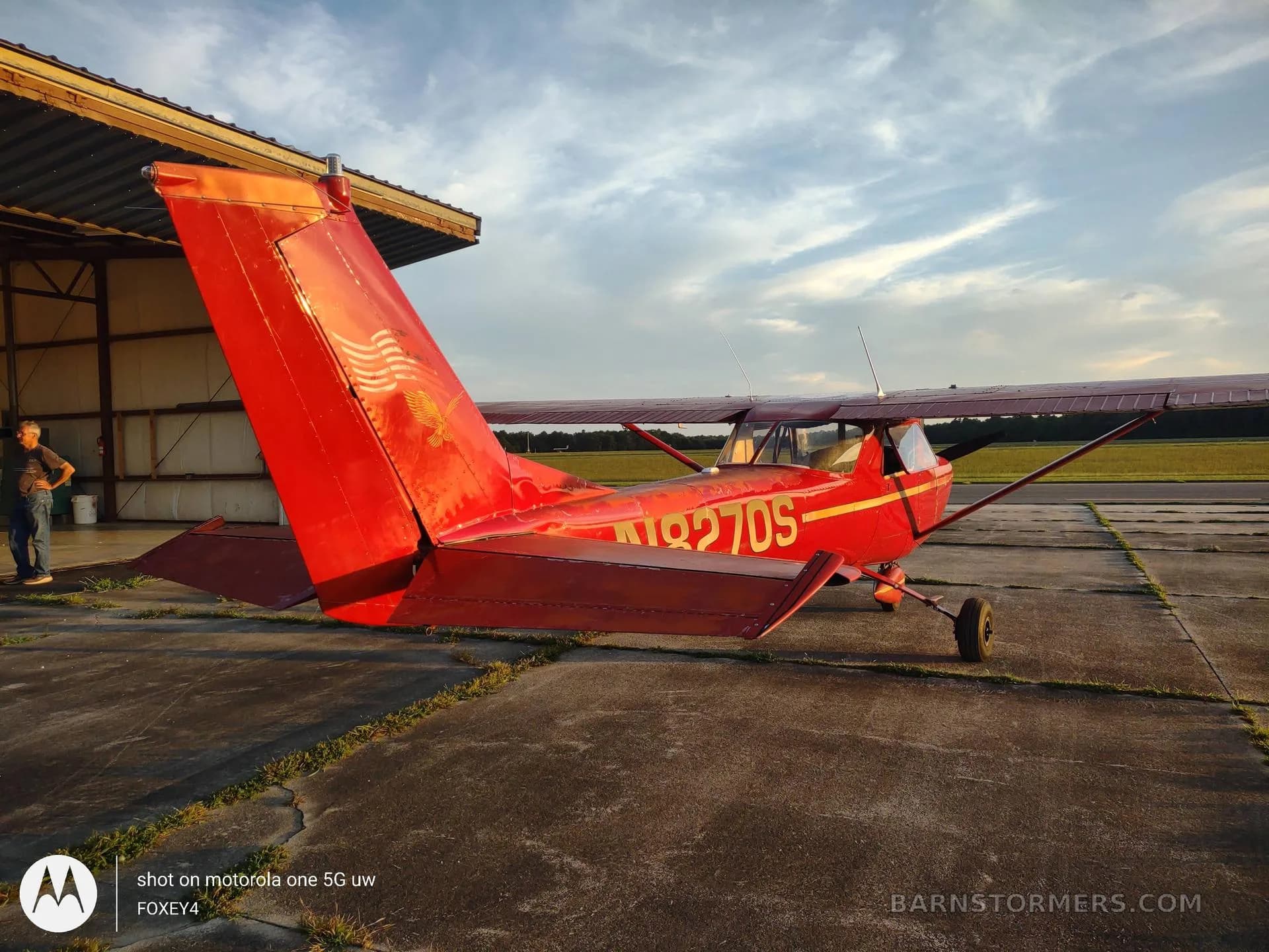 A rear-quarter view of a red Cessna 150 or similar light aircraft with registration N8270S parked outside a hangar.