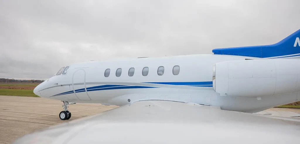 A close-up side view of the front fuselage and wing of a white business jet with blue and silver stripes.