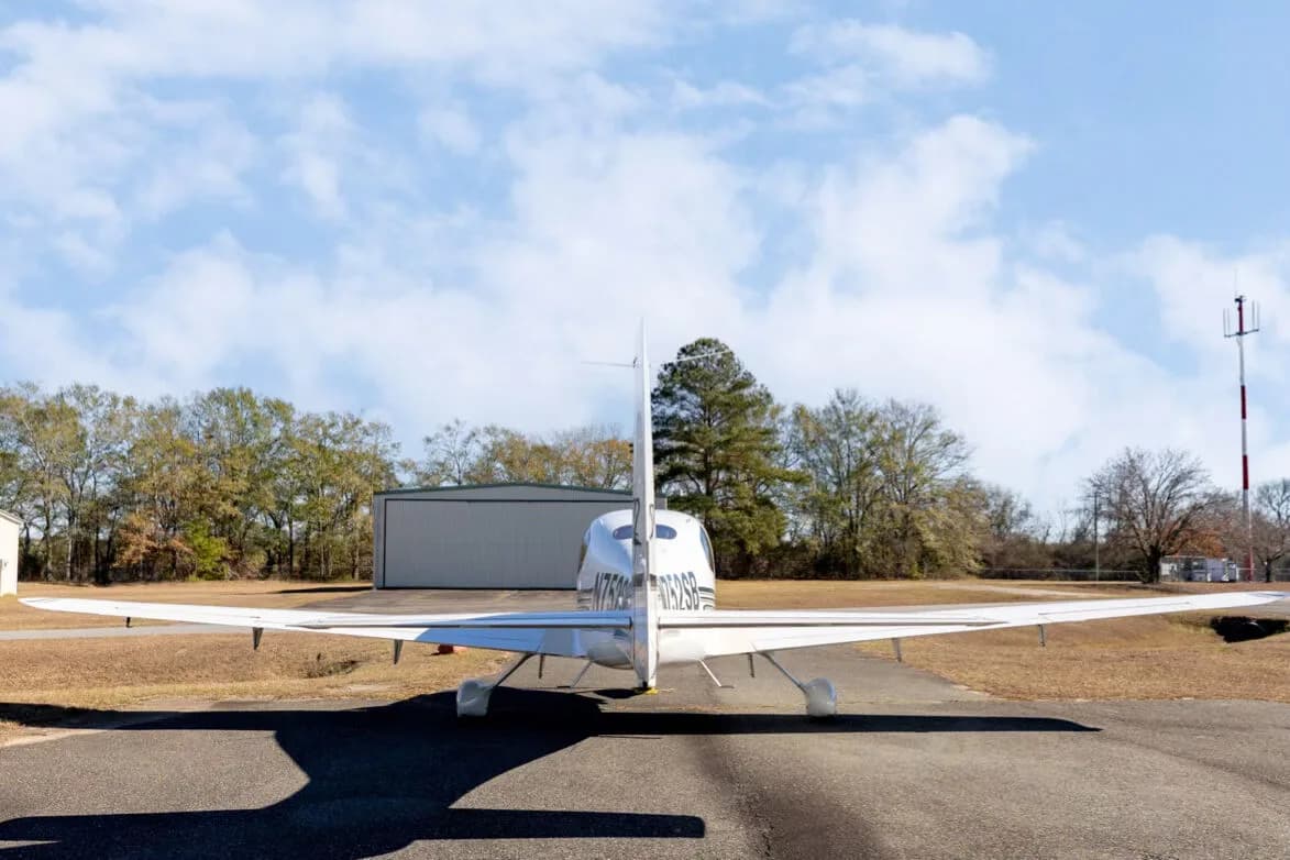 A rear view of the white Cirrus SR22 aircraft, showing its tail and wings, parked on an asphalt ramp.