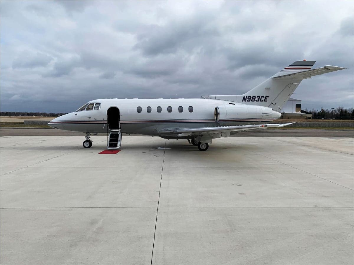 Side view of a white aircraft with the door open on the tarmac.