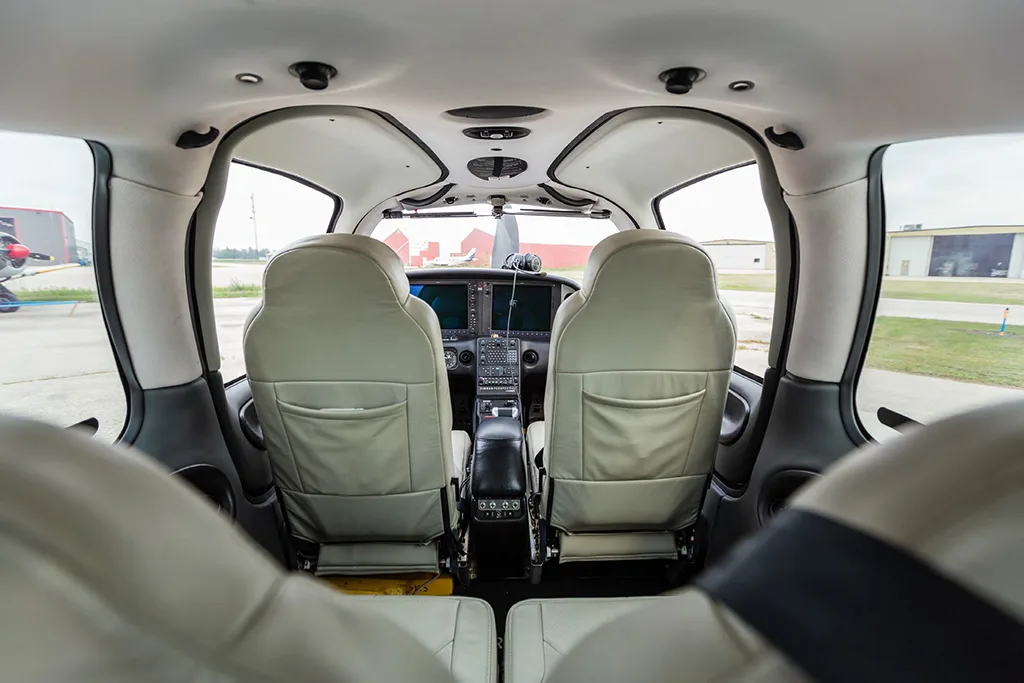 View from the rear seats looking forward into the cockpit of a light aircraft, showing the pilot and co-pilot seats and instrument panel.