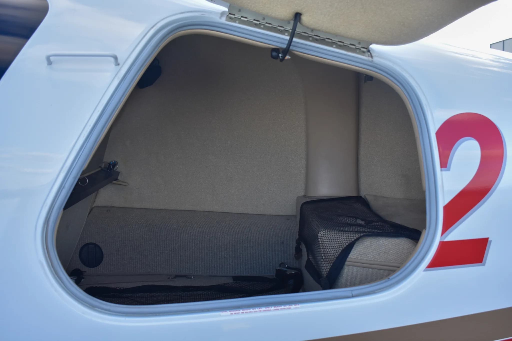View into an open, carpeted baggage compartment of the aircraft, showing a mesh net and storage space.